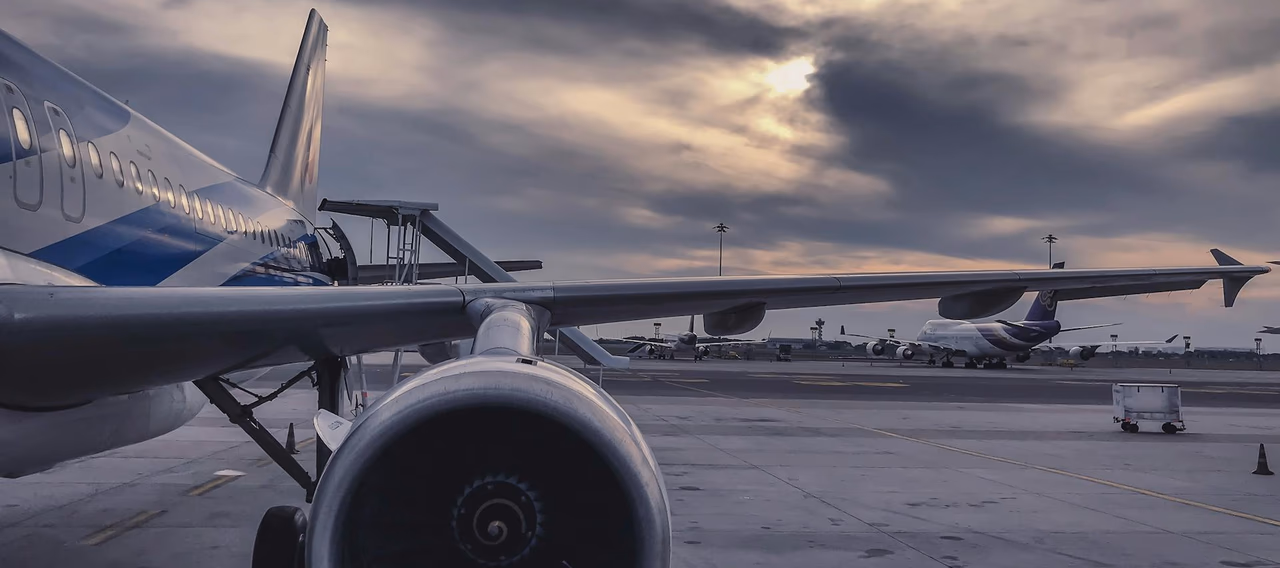 Commercial aircraft parked on an airport tarmac, with engine and wing in view beneath a dramatic cloudy sky